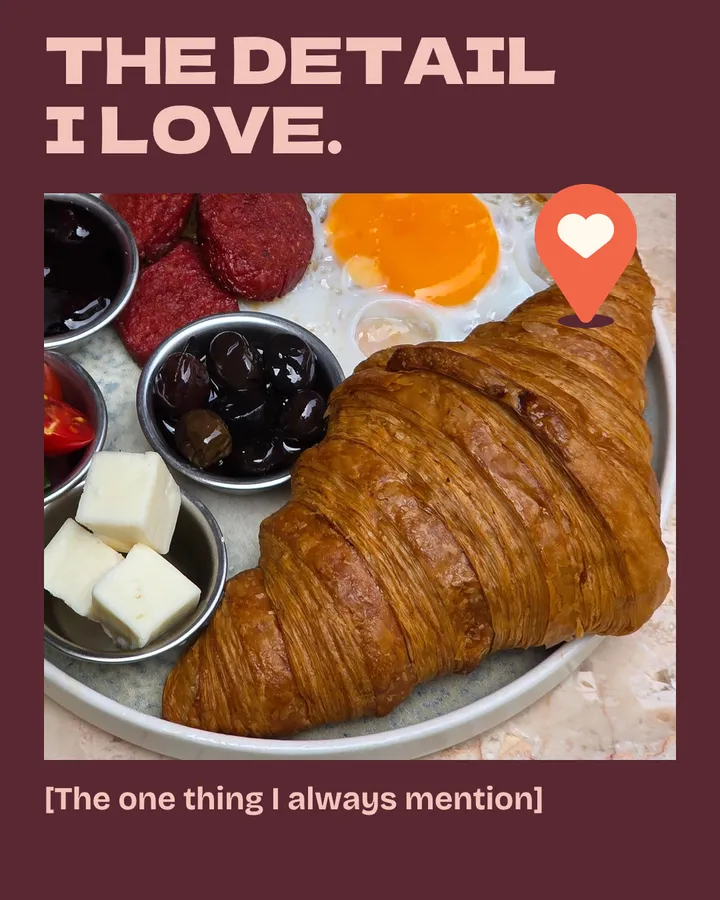 The detail I love. A close view of a buttery croissant on a breakfast plate with a fried egg, olives, cheese and tomatoes on a marble table. The red pin marks the croissant. The one thing I always mention.
